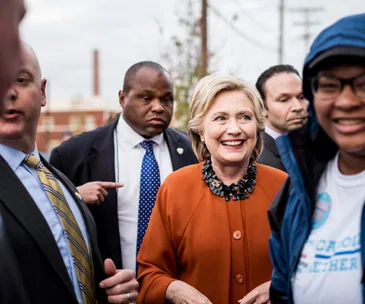 A smiling woman in an orange coat surrounded by people outdoors.