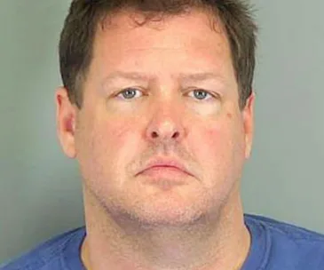 Portrait of an adult male with short hair wearing a blue shirt, looking directly at the camera against a plain background.