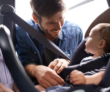 Man smiling at baby in car seat, adjusting the seatbelt.