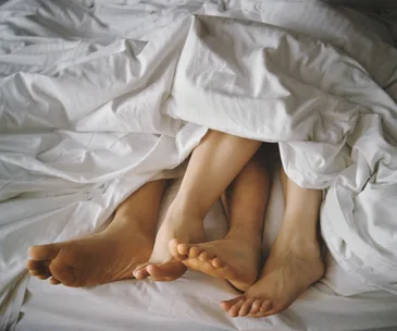 Feet of a couple intertwined under white bed sheets.