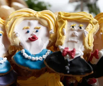 Cookies decorated to resemble political figures with yellow hair and colorful outfits, featuring detailed faces.