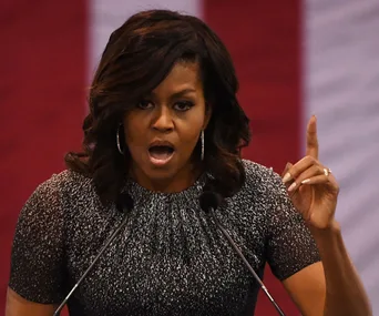 A woman speaking passionately at a podium with a red and white backdrop.