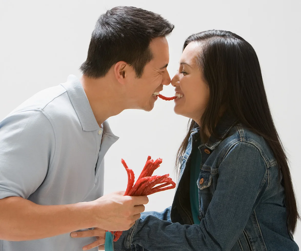 Couple playfully eating red licorice together, smiling and close.