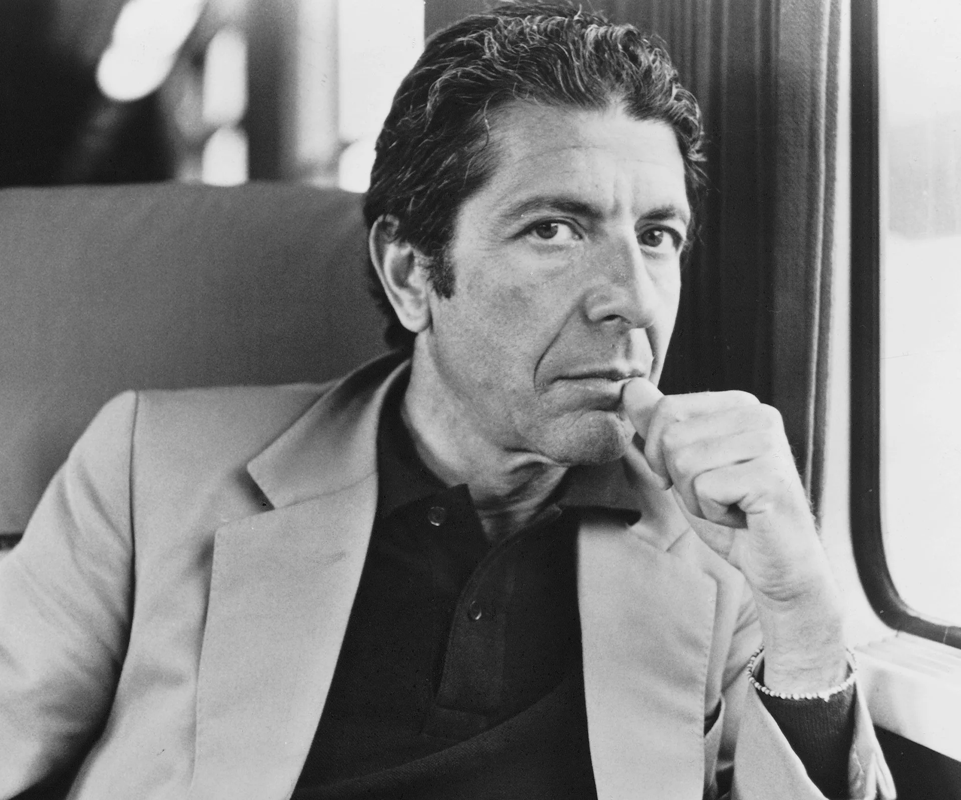 A person in a contemplative pose, sitting in a train with a thoughtful expression, wearing a light-colored jacket.