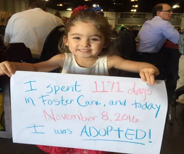 Little girl smiling, holding a sign celebrating her adoption after 1,171 days in foster care on November 8, 2016.