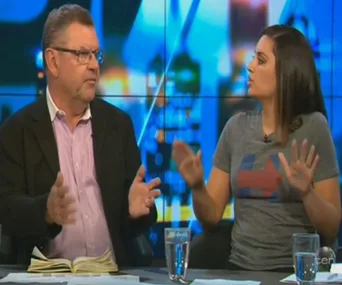 Two people engaged in a discussion on a TV show set, with a background of urban lights.