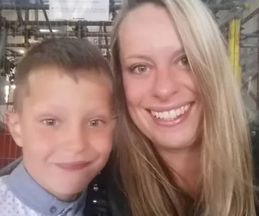 A woman and young boy smiling, close together, in an indoor setting.