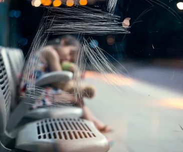 Blurred child holding stuffed animal on scratched bus station bench at night.