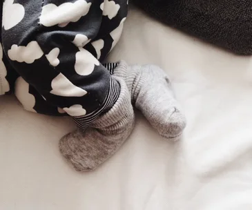 Baby sleeping in cloud-patterned pajamas and gray socks on a white blanket.
