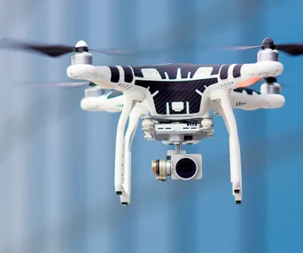 A quadcopter drone with a camera hovers against a blurred blue background.