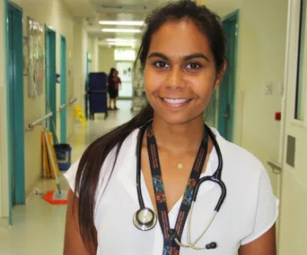 A smiling doctor with a stethoscope in a hospital hallway.