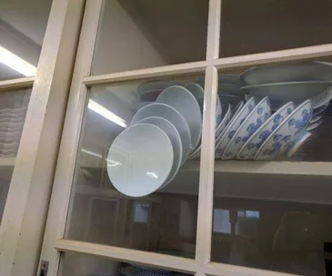 Plates stacked against a glass cupboard door, precariously positioned to fall if opened.