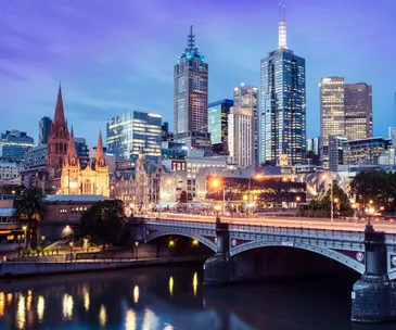 Melbourne cityscape at dusk, featuring St. Paul's Cathedral and modern skyscrapers reflected in the Yarra River.