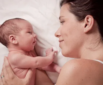 Mother and baby lying on bed, facing each other with tender expressions.