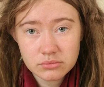 Young woman with long hair, wearing a red scarf, looking directly at the camera in a neutral expression.