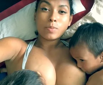 Woman lying down breastfeeding two children simultaneously.