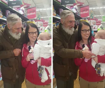 An elderly man, a woman, and a baby stand smiling together in a store toy aisle.