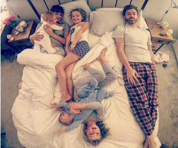 Family of six lounging on a bed, capturing a relaxed and playful moment together.