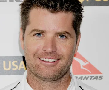 Man smiling at an event with logos in the background.