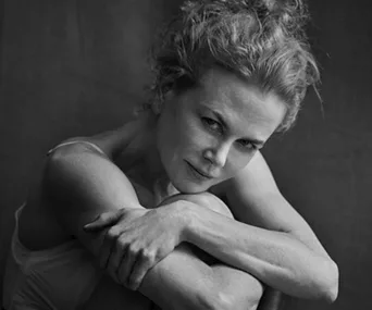 A person with light hair and a thoughtful expression, seated and hugging their knees in a black and white photograph.
