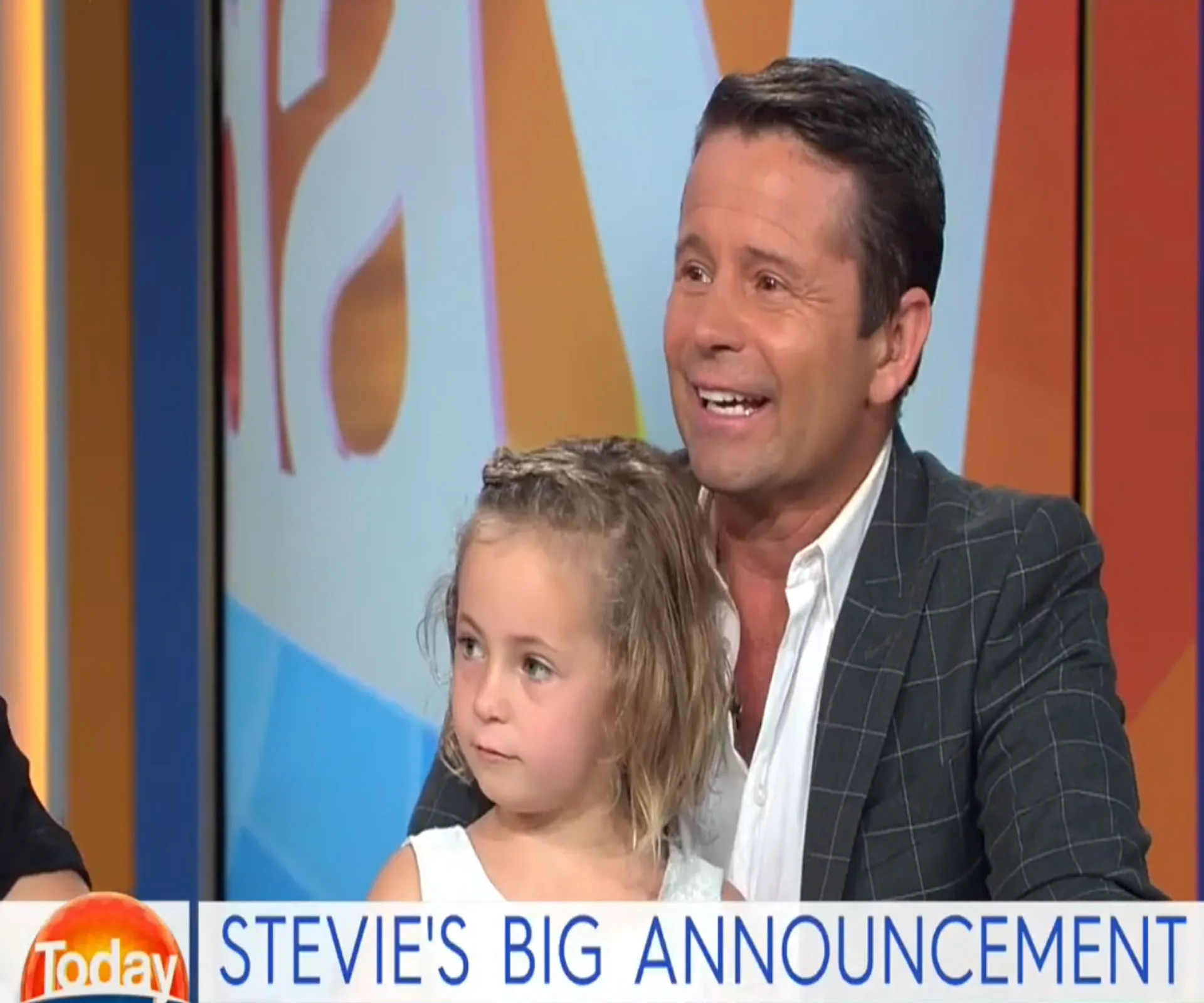 Man smiling with a young girl on a TV show set, text reads "Stevie's Big Announcement".