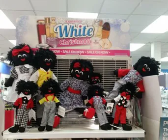 Dolls with black faces and colorful outfits on a store display with "White Christmas" signage above.