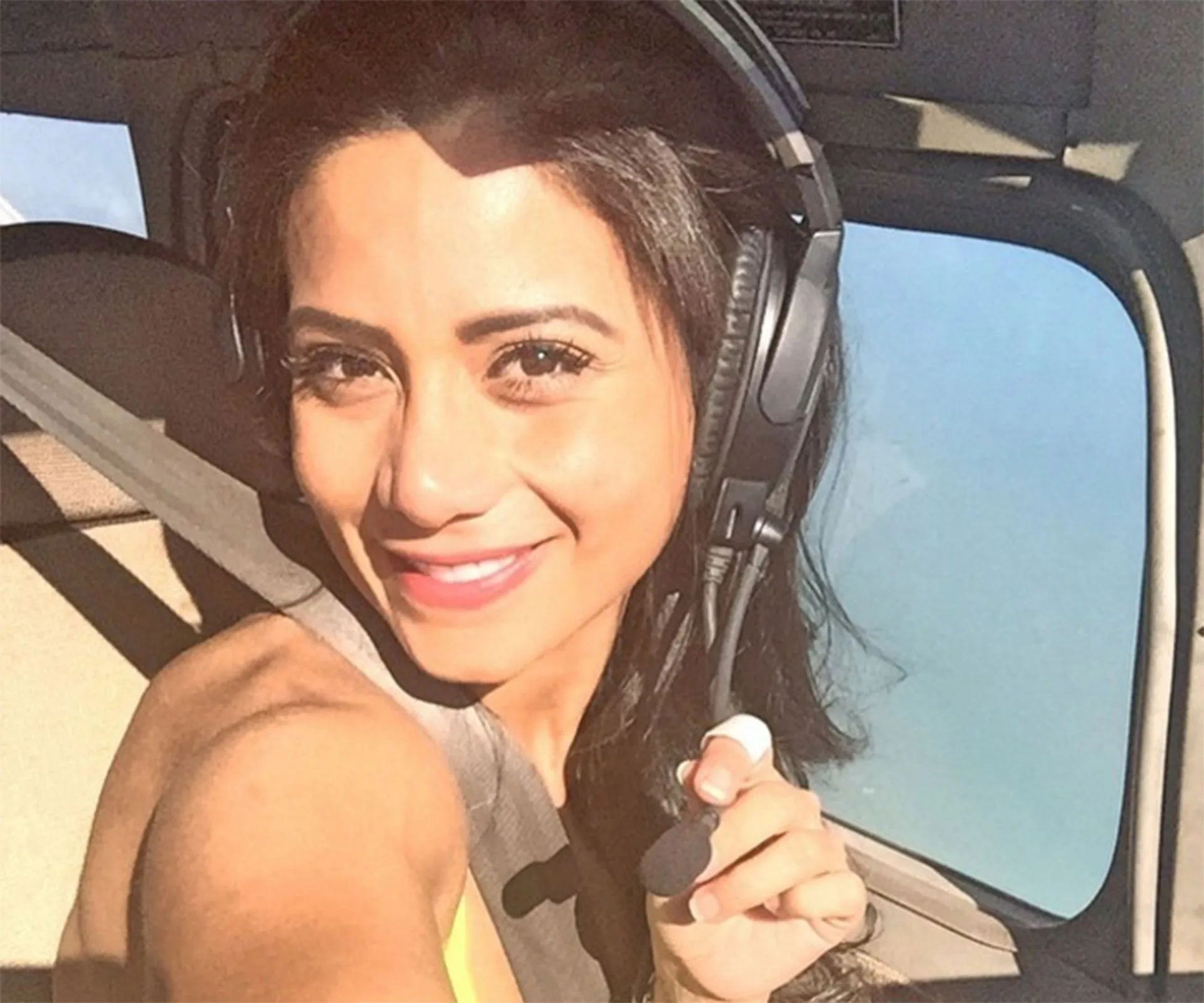 A person wearing a headset smiles in a plane cockpit with a clear sky visible outside.