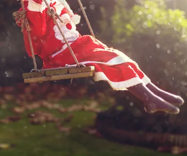 Child in Santa costume swinging outdoors in sunny garden.