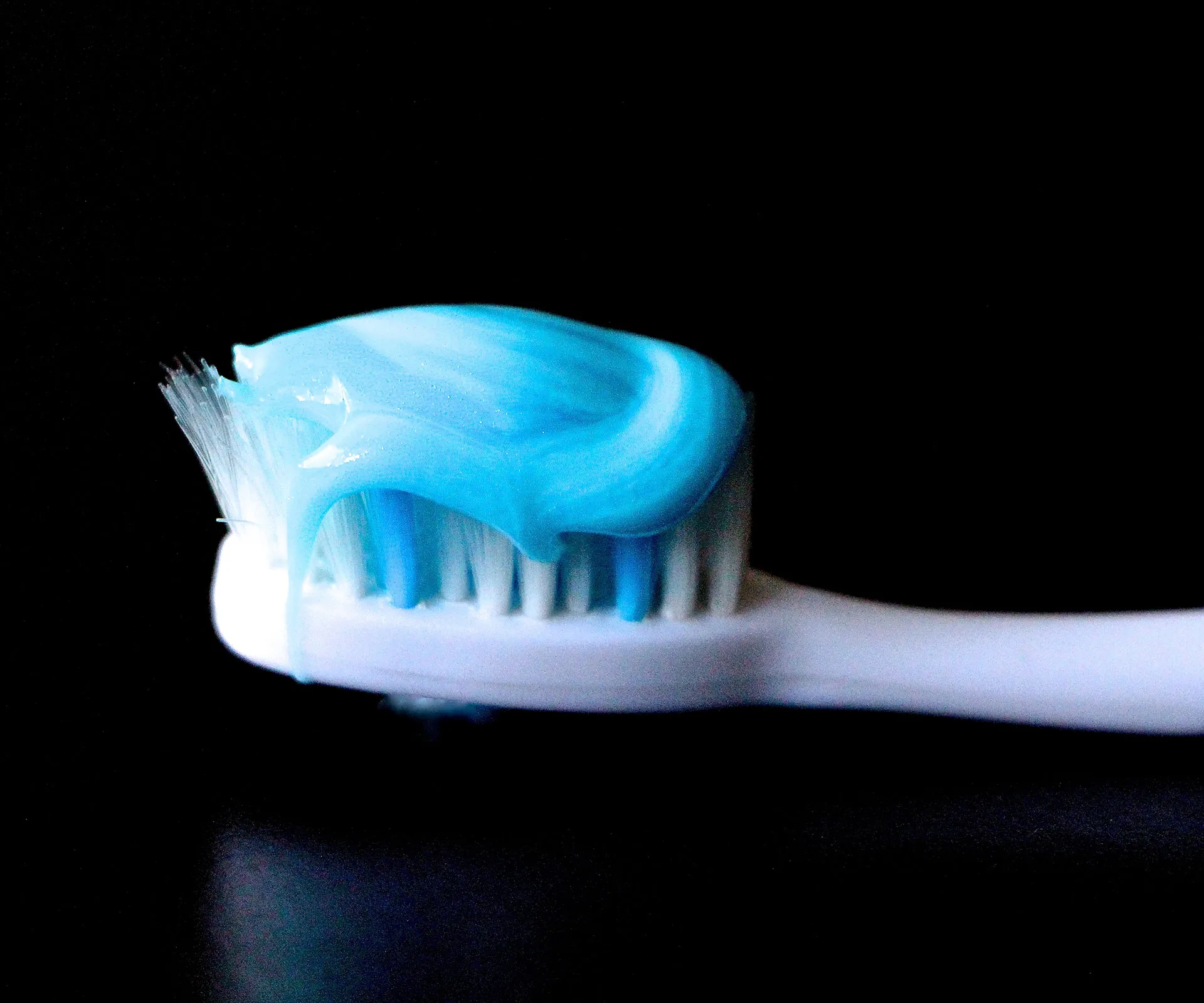 A toothbrush with blue toothpaste against a black background.
