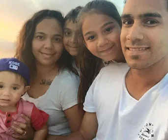 A smiling family of five, including two parents and three children, posing for a selfie.