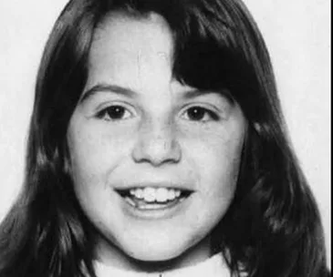 A black and white photo of a young girl with long hair smiling.