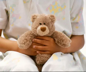 Child in patterned pajamas holding a brown teddy bear.