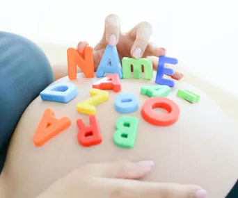 Colorful alphabet letters spelling "NAME" on a pregnant belly.