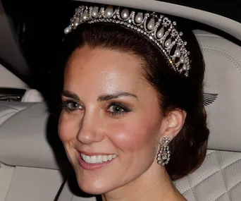 A woman wearing a pearl and diamond tiara smiles in a close-up portrait inside a car.