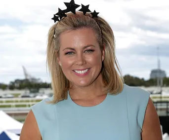 Blonde woman smiling, wearing a blue dress and a black star headband, standing outdoors with blurred background.