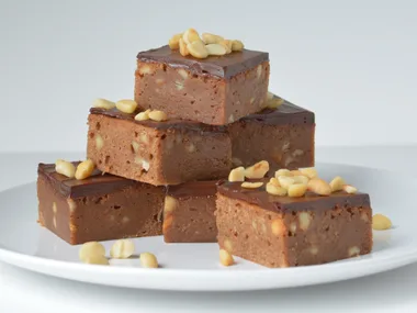 Milk chocolate and macadamia brownies stacked on a white plate, topped with nuts, showing a rich fudgy texture.
