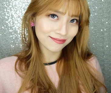 A woman with long blonde hair and pink lipstick smiles against a silver glitter background.