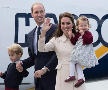 A family of four, smartly dressed, waves while standing in front of an airplane.