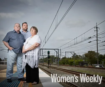 Three people stand solemnly on a train platform, beneath overhead power lines, with "The Australian Women's Weekly" text.