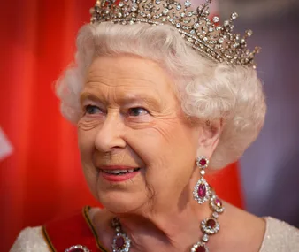 A woman wearing an ornate tiara and matching ruby and diamond jewelry, against a softly blurred background.