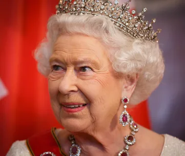 A woman wearing an ornate tiara and matching ruby and diamond jewelry, against a softly blurred background.