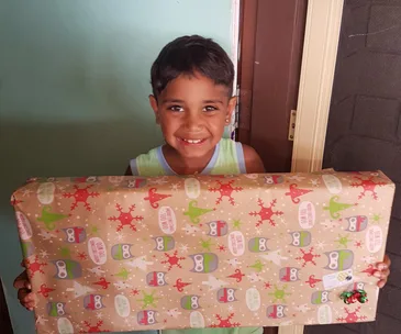 Boy smiling while holding a large, wrapped gift with festive design.