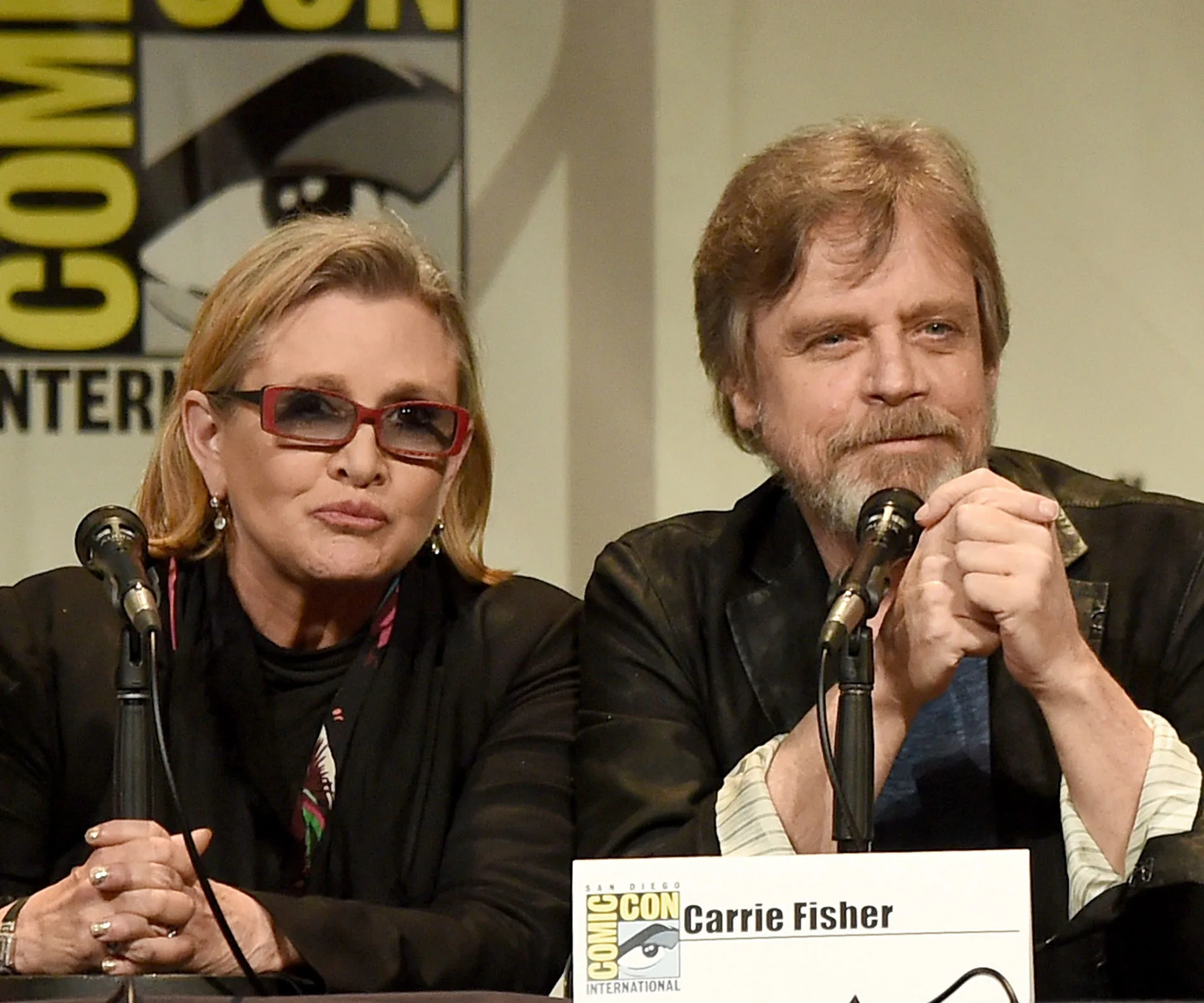 Carrie Fisher and Mark Hamill at San Diego Comic-Con panel, sitting at a table with microphones in front of them.