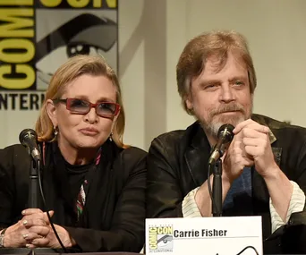 Carrie Fisher and Mark Hamill at San Diego Comic-Con panel, sitting at a table with microphones in front of them.