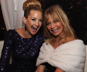 Two women smiling and embracing each other at an event, with one wearing a blue sequined dress.