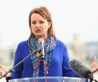 Woman speaking at a podium with a microphone, wearing a blue top and patterned scarf.