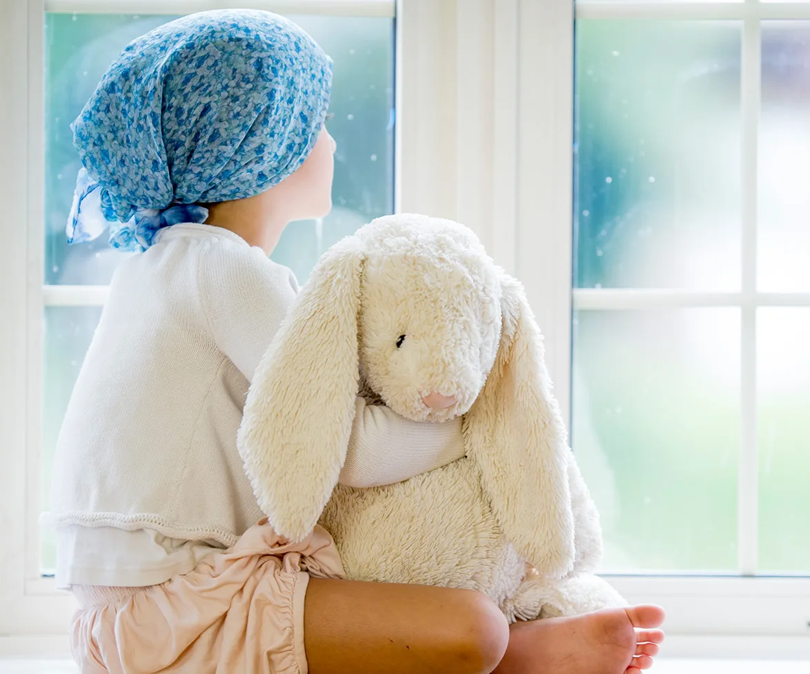 Little girl with cancer stares out window of hospital.