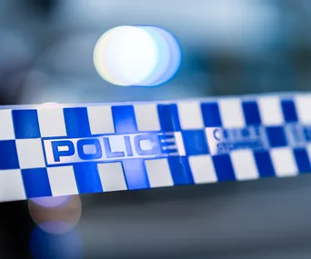 Police tape with blue and white check pattern, blurred police lights in background.