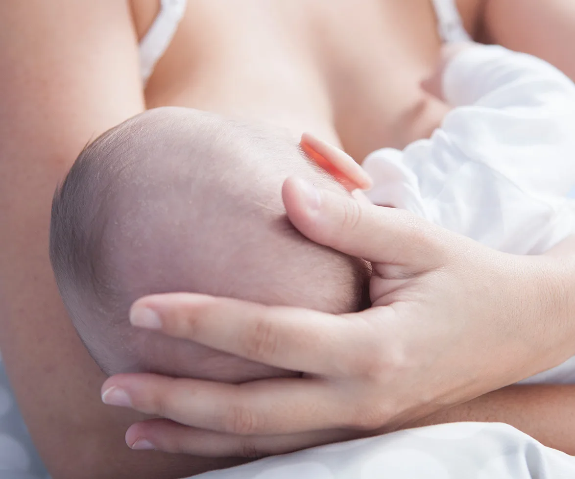 A baby being breastfed, with a close-up of a mother's hand gently cradling the baby's head.