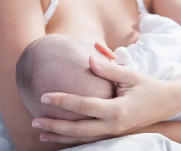 A baby being breastfed, with a close-up of a mother's hand gently cradling the baby's head.